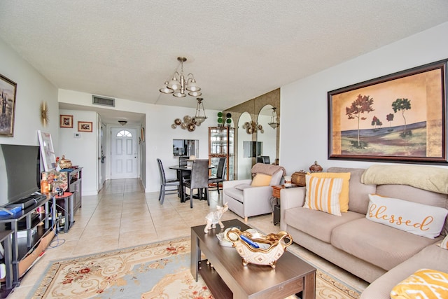 living area featuring light tile patterned floors, a textured ceiling, visible vents, and a notable chandelier