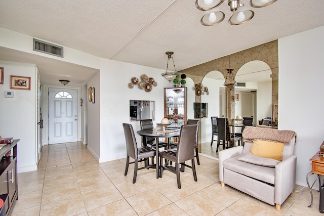 dining area featuring light tile patterned floors, baseboards, visible vents, arched walkways, and a textured ceiling