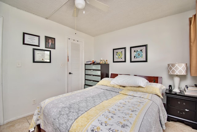 bedroom featuring light tile patterned floors, baseboards, ceiling fan, a textured ceiling, and a closet