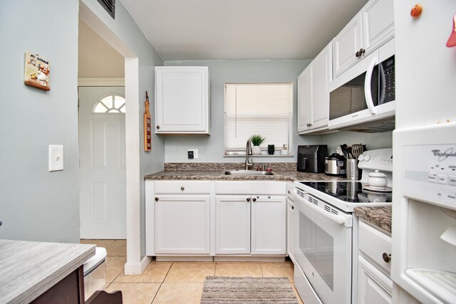 kitchen with white appliances, light tile patterned floors, dark countertops, white cabinetry, and a sink