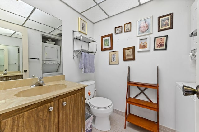 bathroom featuring vanity, toilet, a paneled ceiling, and stacked washer / drying machine