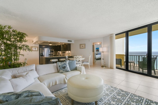 living room featuring light tile patterned flooring, a water view, and a textured ceiling