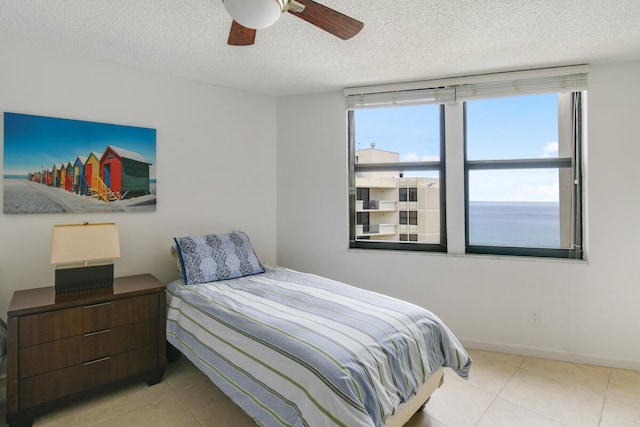 bedroom featuring ceiling fan, a water view, light tile patterned floors, and a textured ceiling