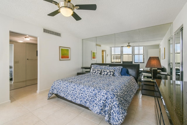 bedroom featuring ceiling fan, a closet, light tile patterned floors, and a textured ceiling