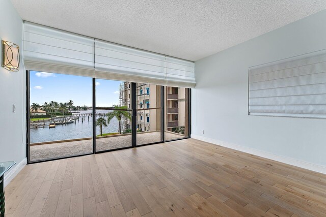 spare room with a textured ceiling, a water view, hardwood / wood-style floors, and expansive windows