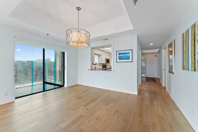 unfurnished living room featuring plenty of natural light, light hardwood / wood-style flooring, and a tray ceiling