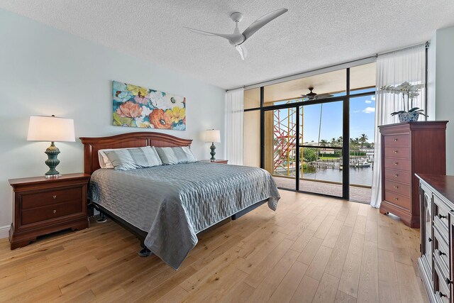 bedroom with a textured ceiling, light hardwood / wood-style flooring, floor to ceiling windows, access to exterior, and ceiling fan