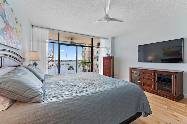 bedroom featuring a textured ceiling, floor to ceiling windows, access to exterior, hardwood / wood-style flooring, and ceiling fan