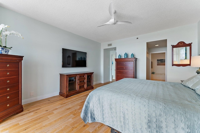 bedroom with light wood-type flooring, ceiling fan, ensuite bathroom, and a textured ceiling