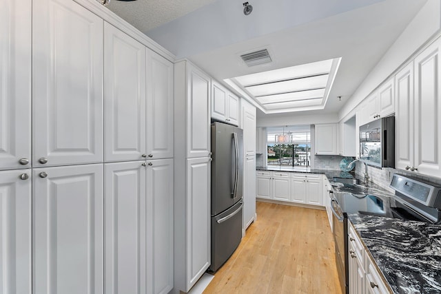 kitchen featuring light hardwood / wood-style flooring, appliances with stainless steel finishes, sink, dark stone countertops, and white cabinets