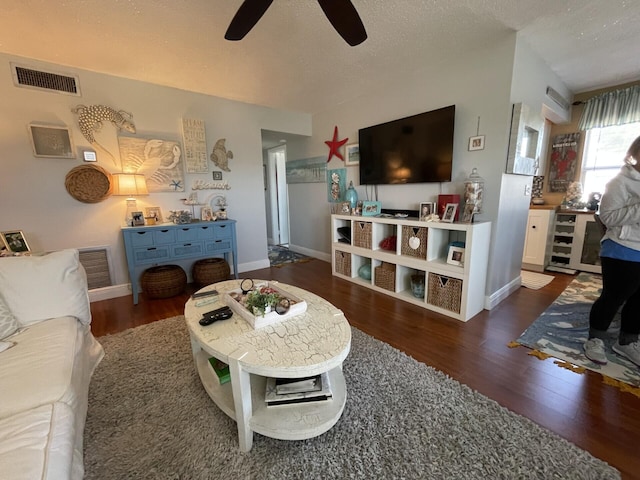 living room featuring dark wood-type flooring, a textured ceiling, and ceiling fan