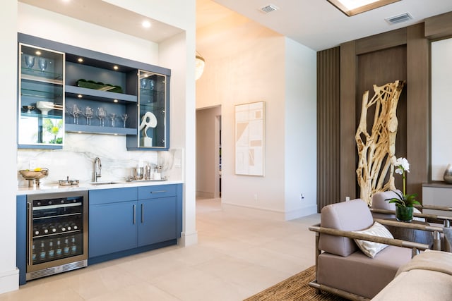 bar with sink, backsplash, blue cabinetry, and beverage cooler