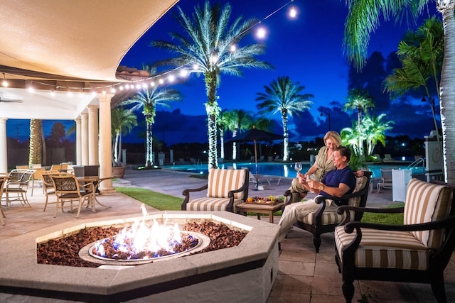 patio at night featuring a community pool and an outdoor fire pit