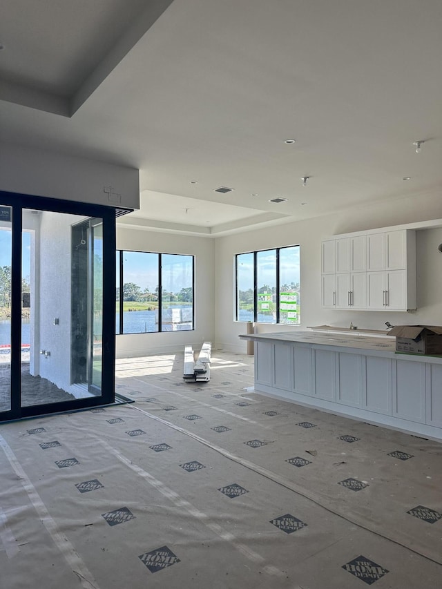 kitchen with a raised ceiling, white cabinets, and a water view