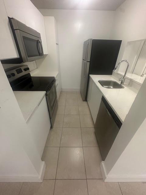 kitchen featuring light countertops, light tile patterned floors, white cabinets, stainless steel appliances, and a sink