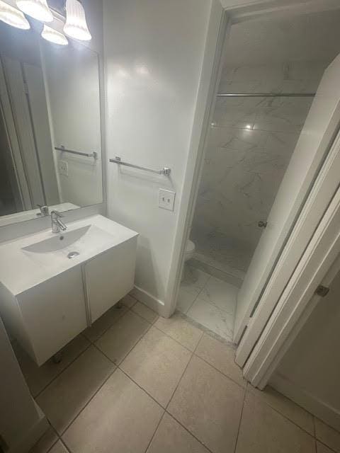 full bathroom featuring vanity, toilet, baseboards, and a marble finish shower