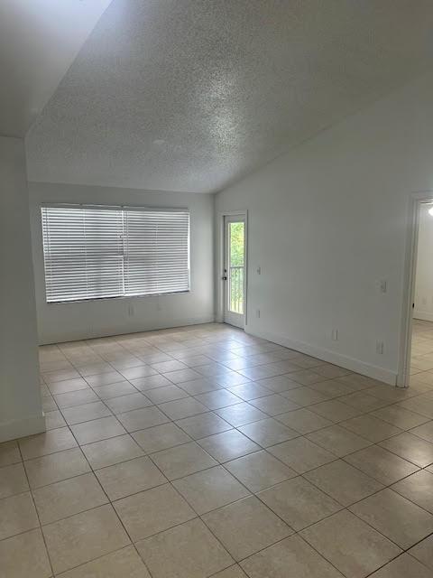 tiled spare room with a textured ceiling and vaulted ceiling