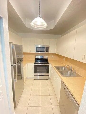 kitchen with appliances with stainless steel finishes, light tile patterned floors, a raised ceiling, and sink