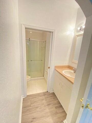 bathroom featuring vanity, toilet, wood-type flooring, and a shower with shower door