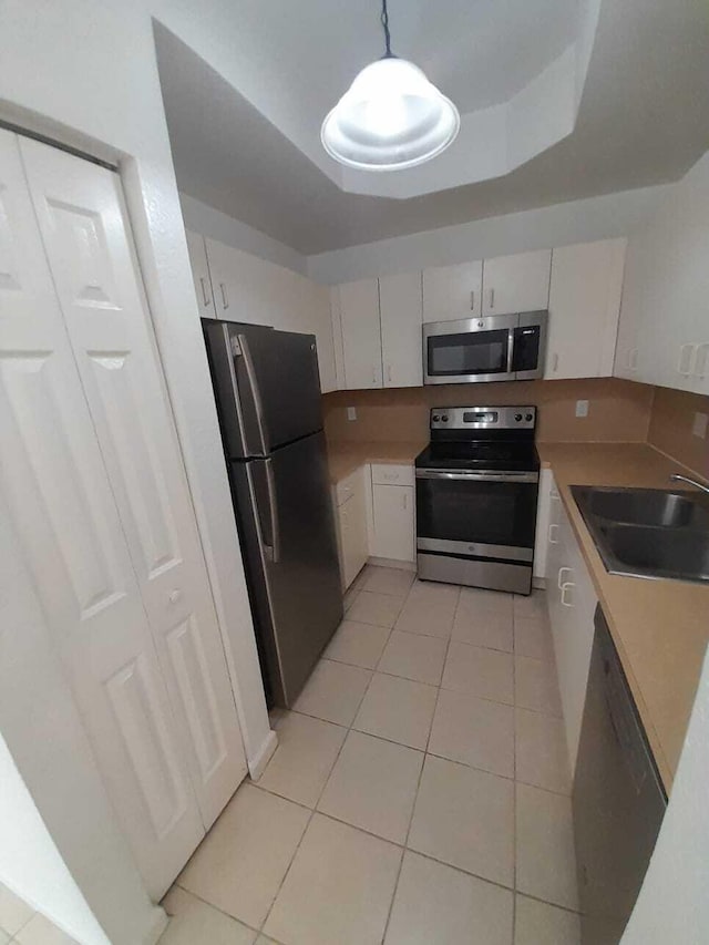 kitchen with white cabinets, hanging light fixtures, stainless steel appliances, sink, and light tile patterned flooring