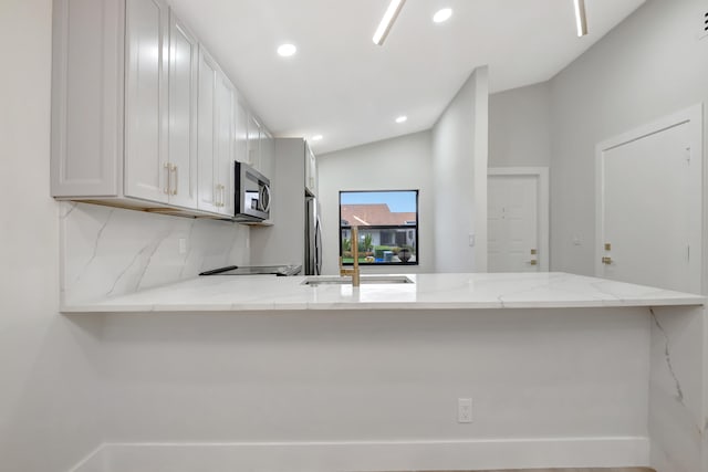 kitchen with kitchen peninsula, white cabinetry, stainless steel appliances, light stone countertops, and vaulted ceiling