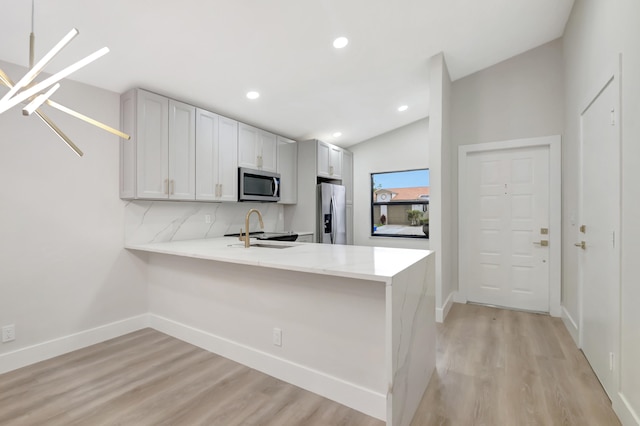 kitchen with light hardwood / wood-style floors, stainless steel appliances, kitchen peninsula, lofted ceiling, and white cabinetry