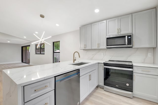 kitchen featuring pendant lighting, sink, kitchen peninsula, stainless steel appliances, and light hardwood / wood-style floors