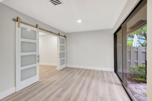 empty room with built in shelves, a barn door, and light hardwood / wood-style flooring