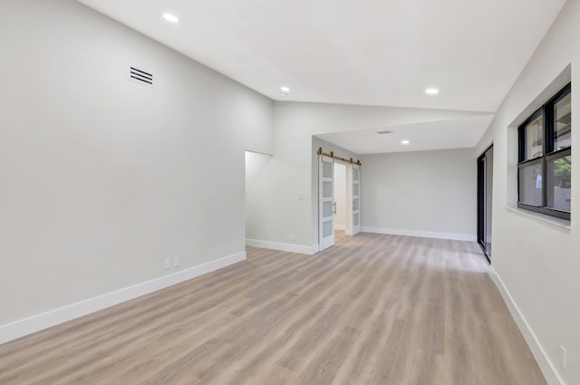 spare room with light wood-type flooring, a barn door, and vaulted ceiling