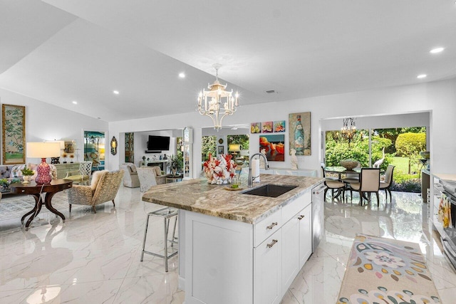 kitchen featuring a kitchen island with sink, sink, a chandelier, white cabinetry, and light stone counters