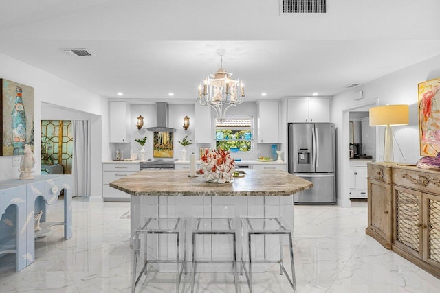 kitchen with a kitchen breakfast bar, wall chimney exhaust hood, pendant lighting, appliances with stainless steel finishes, and white cabinetry