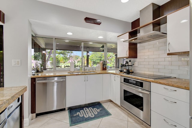 kitchen featuring a textured ceiling, stainless steel appliances, wall chimney range hood, sink, and white cabinetry