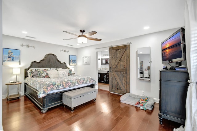 bedroom with connected bathroom, a barn door, ceiling fan, and hardwood / wood-style flooring