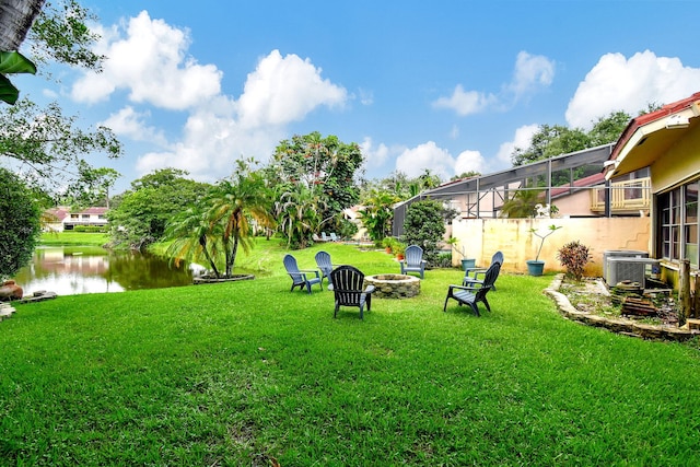 view of yard featuring a water view, a fire pit, cooling unit, and a lanai