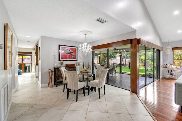 dining space with a textured ceiling, lofted ceiling, light hardwood / wood-style flooring, and a chandelier