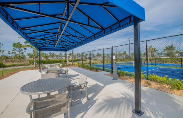 view of patio with a tennis court and fence