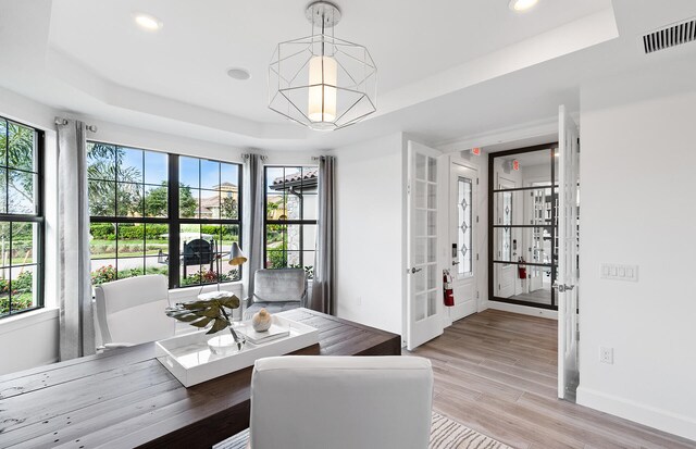 dining space featuring light wood finished floors, visible vents, a raised ceiling, and baseboards