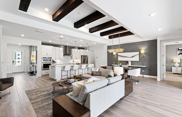 living area with visible vents, brick wall, baseboards, beam ceiling, and light wood-style floors