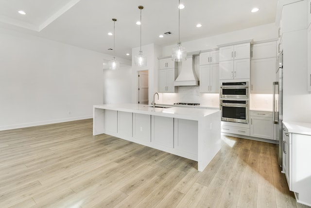 kitchen featuring sink, premium range hood, stainless steel double oven, and an island with sink