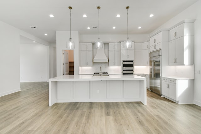 kitchen with a spacious island, stainless steel appliances, decorative light fixtures, custom exhaust hood, and light hardwood / wood-style floors