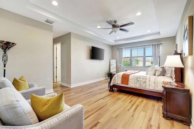 bedroom with ceiling fan, light wood-type flooring, and a tray ceiling