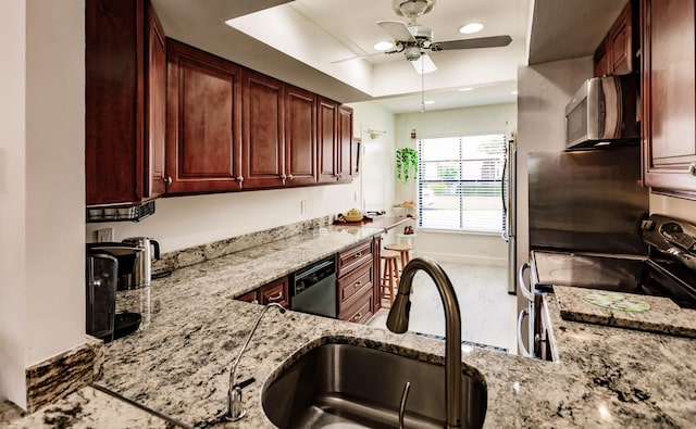 kitchen featuring a tray ceiling, light stone counters, sink, appliances with stainless steel finishes, and ceiling fan