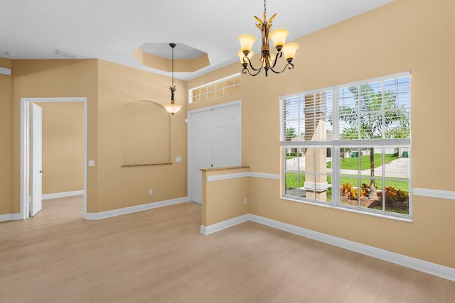 unfurnished room with a tray ceiling, a notable chandelier, and hardwood / wood-style flooring