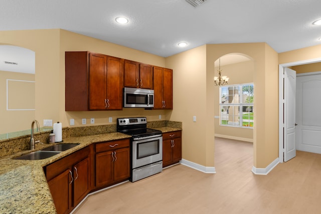 kitchen with appliances with stainless steel finishes, a chandelier, light stone counters, and sink