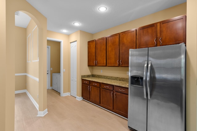 kitchen featuring light wood-type flooring, light stone countertops, washer and dryer, stainless steel fridge, and a textured ceiling