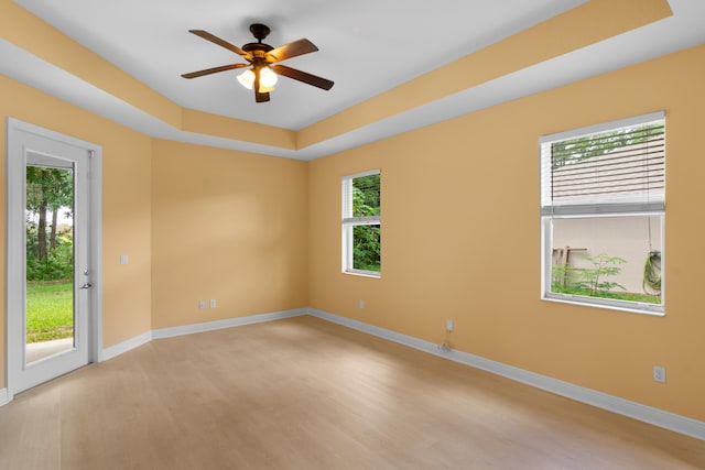 unfurnished room with light wood-type flooring, a raised ceiling, and ceiling fan