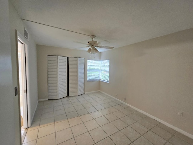 unfurnished bedroom with a textured ceiling, light tile patterned flooring, ceiling fan, and a closet