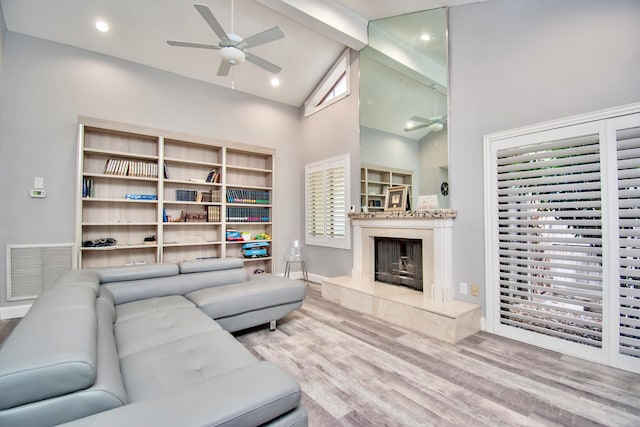 living room featuring a fireplace, beam ceiling, light hardwood / wood-style floors, high vaulted ceiling, and ceiling fan