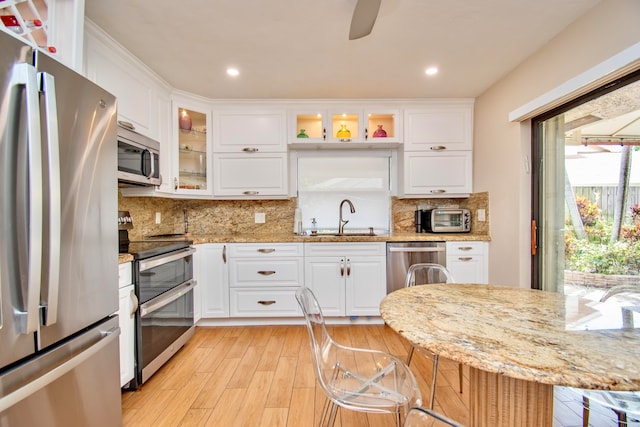 kitchen featuring appliances with stainless steel finishes, light stone counters, light hardwood / wood-style floors, white cabinetry, and sink