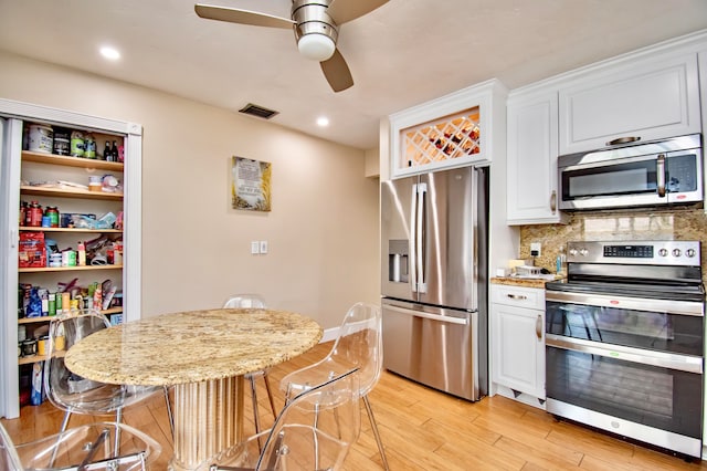 kitchen with white cabinets, appliances with stainless steel finishes, light hardwood / wood-style floors, ceiling fan, and tasteful backsplash